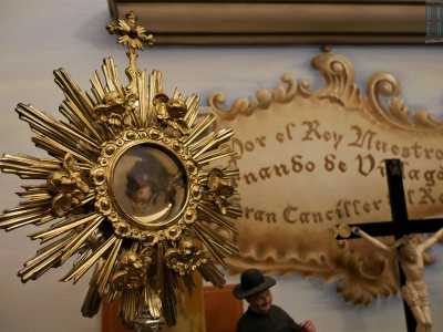 Una consolle ospita vari oggetti votivi o religiosi: un libro di preghiere, un ostensorio al cui interno si intravede una reliquia...